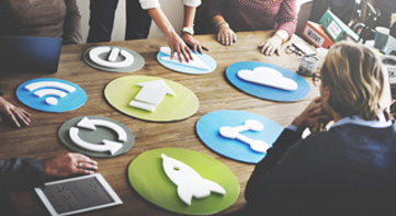 People sitting or standing around a table with communication boards lying on the table